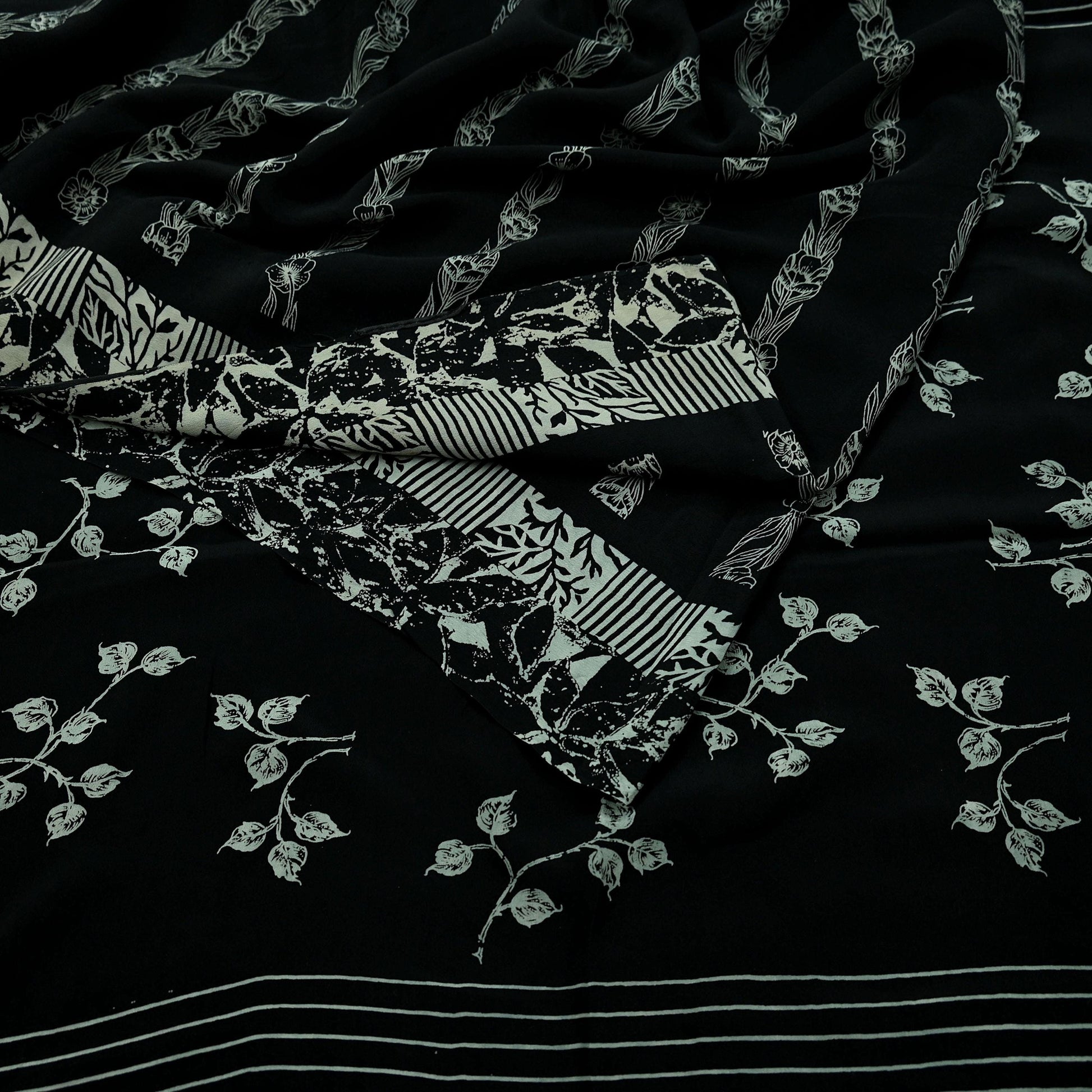 Close-up of black pure crepe silk saree fabric with white floral print on a dark background