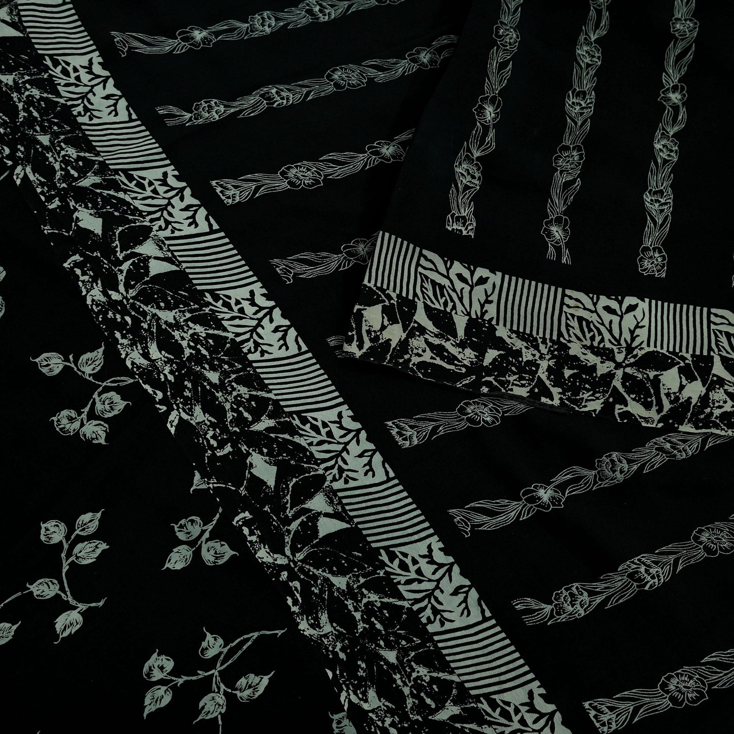 Close-up of black pure crepe silk saree fabric with white floral and stripe patterns on a dark background