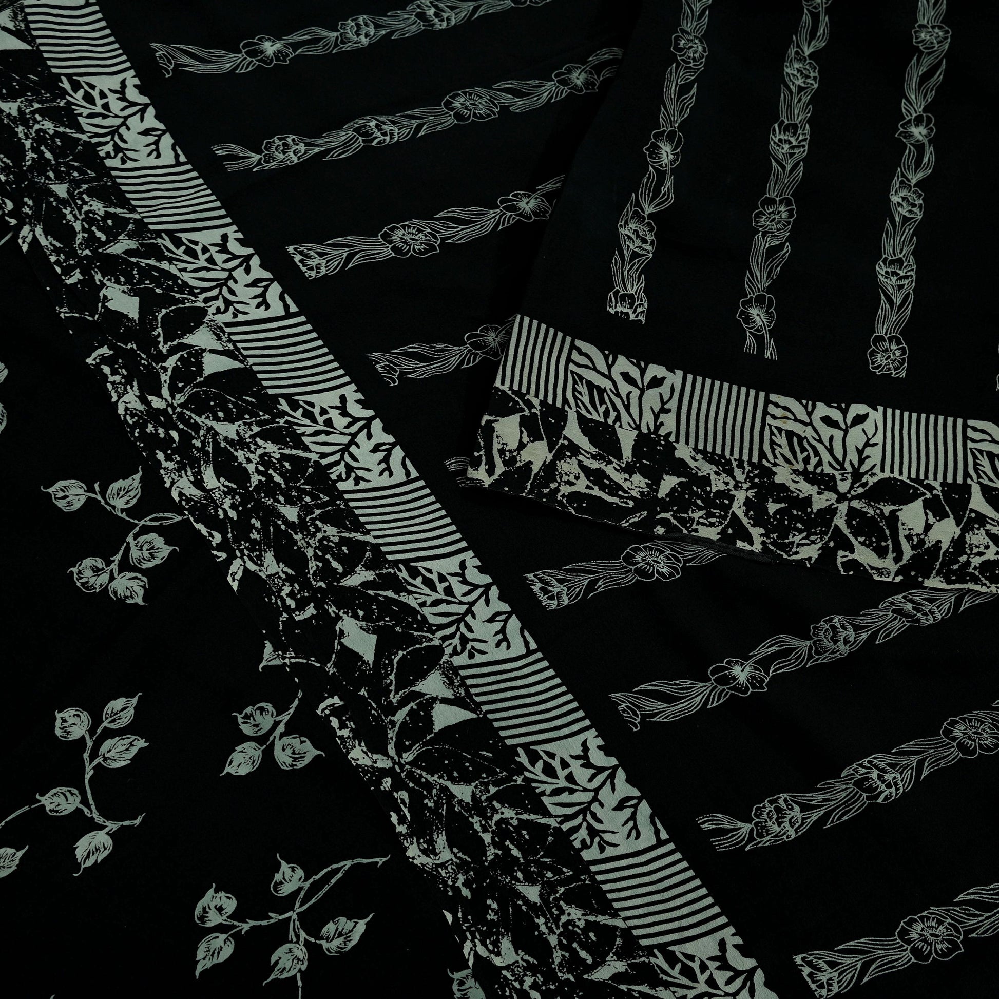 Close-up of black pure crepe silk saree fabric with white floral and stripe patterns on a dark background