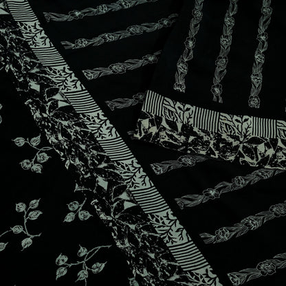 Close-up of black pure crepe silk saree fabric with white floral and stripe patterns on a dark background