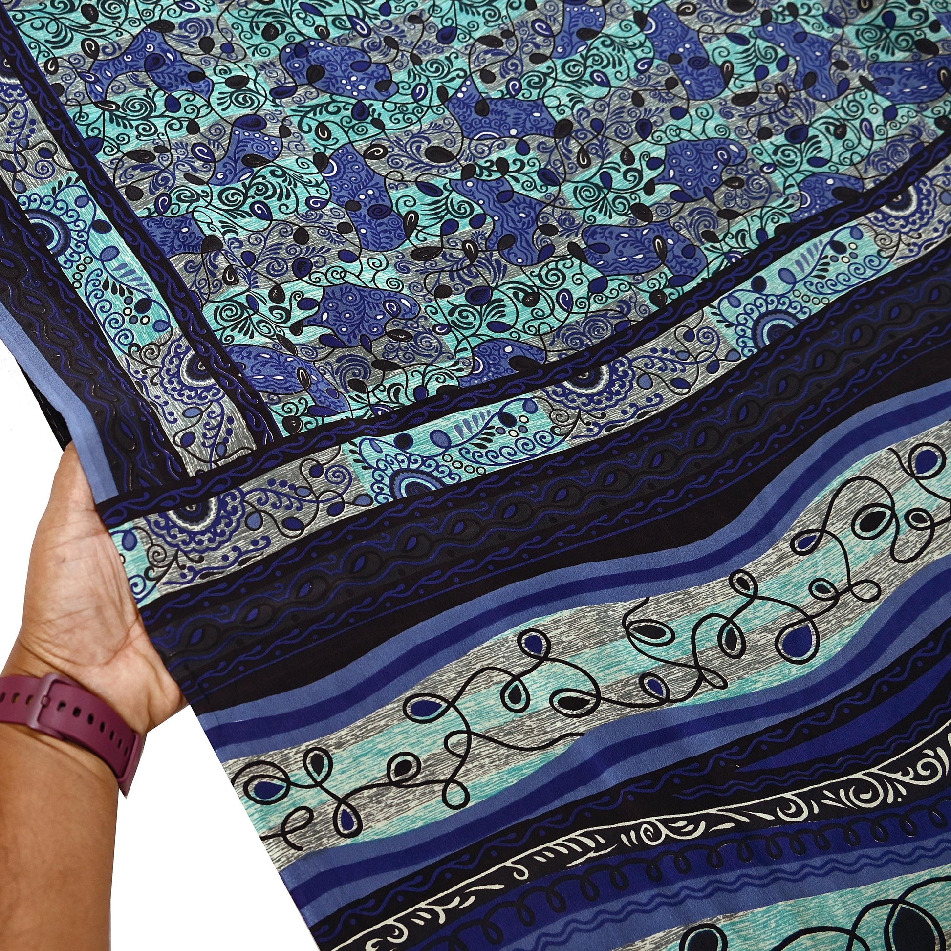 Close-up of a pure crepe silk saree fabric with blue and green pattern, held by a hand.