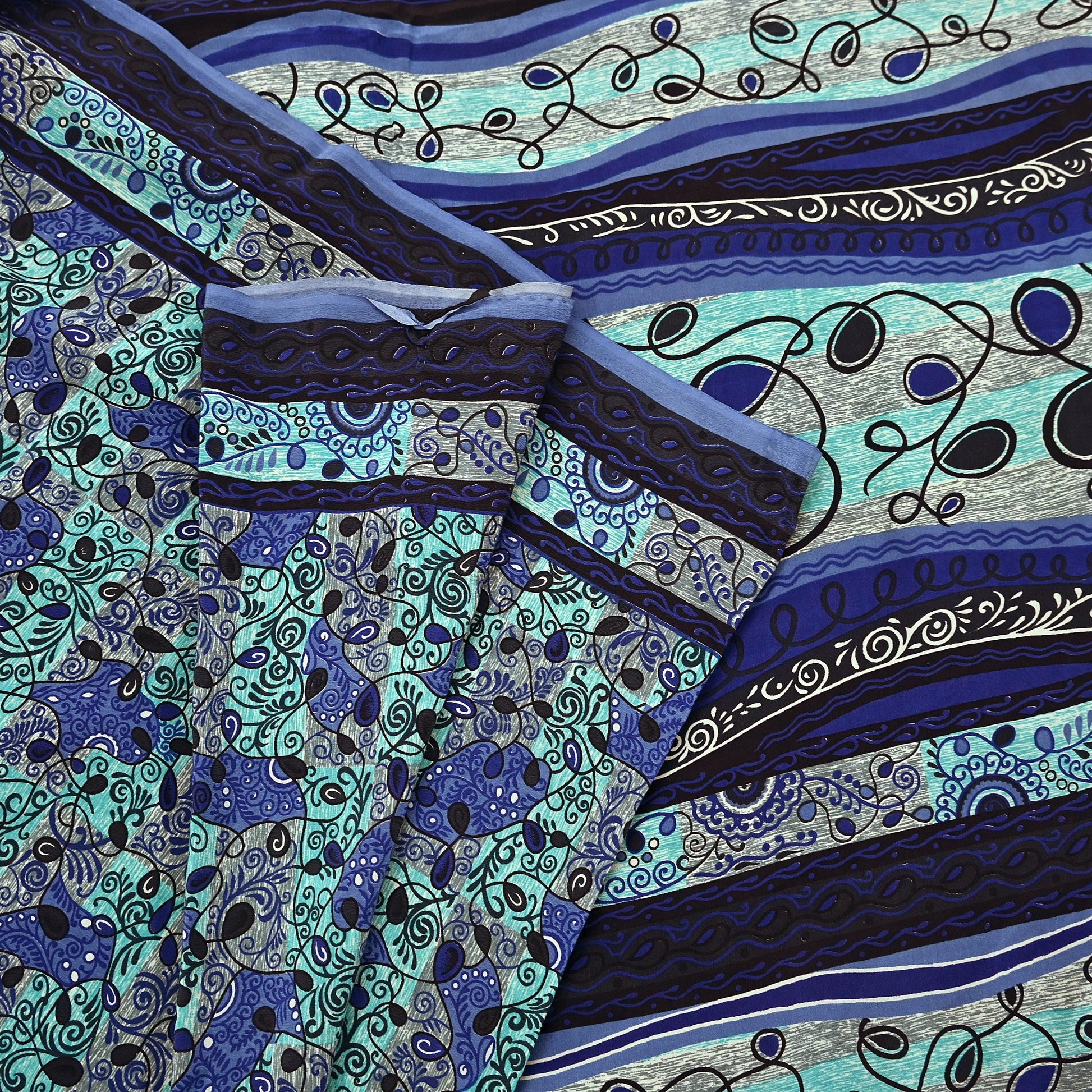 Close-up of a patterned pure crepe silk saree fabric with blue, green, and black colors.