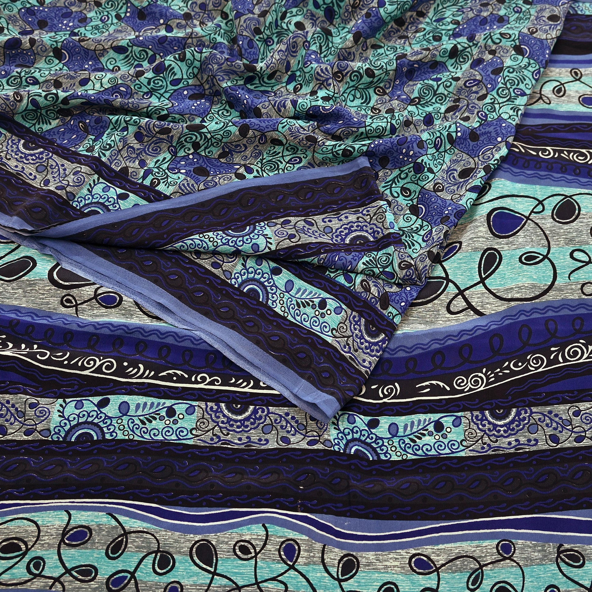 Patterned pure crepe silk saree fabric with blue and green designs on a flat surface