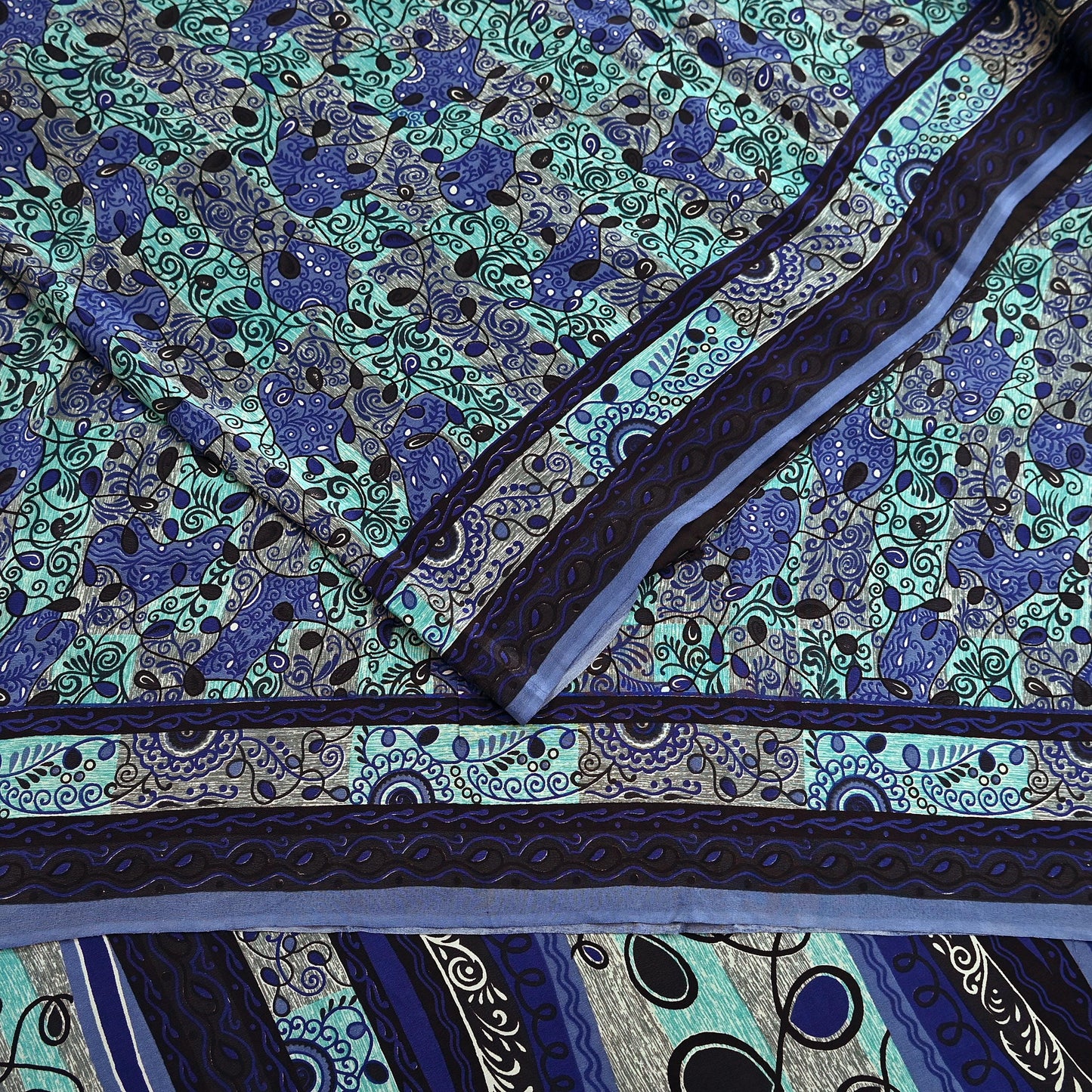 Close-up of a patterned pure crepe silk saree fabric with blue and green design