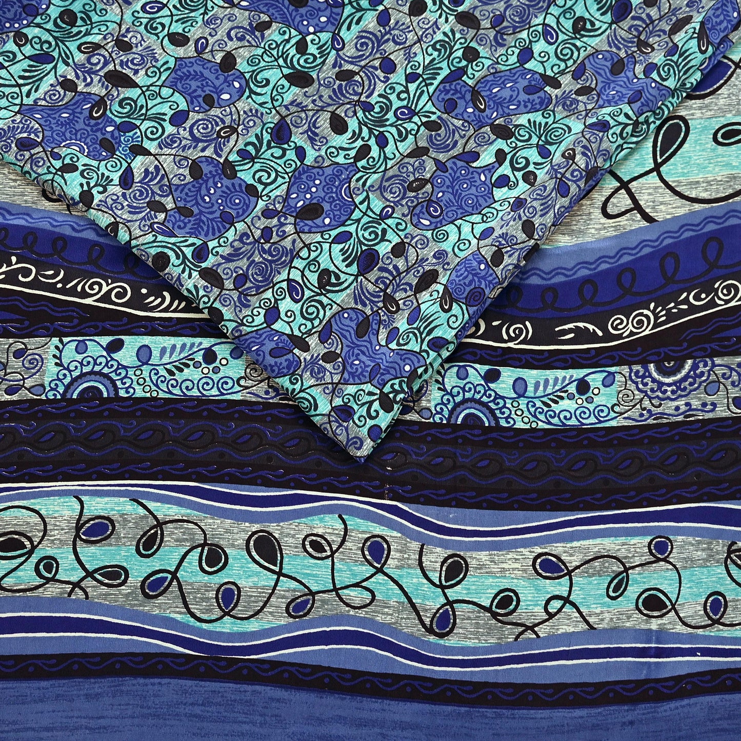 Creative shot of a blue and green pure crepe silk saree fabric with intricate prints.