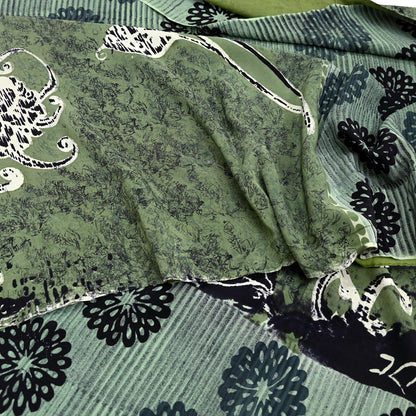 Green pure crepe silk saree fabric with black floral patterns and white abstract designs.